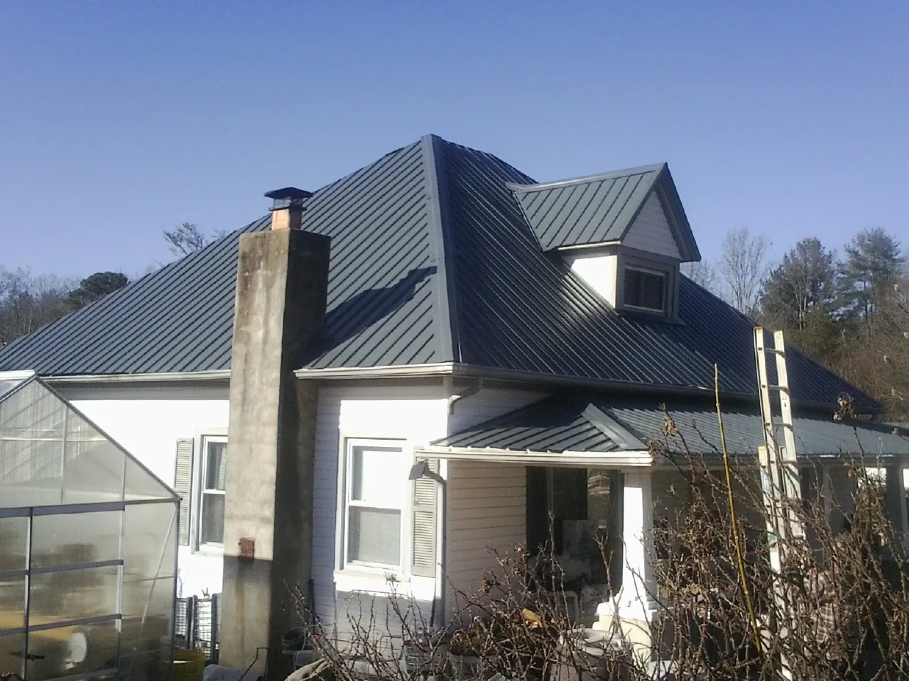 Dark blue standing seam metal roof on a white farmhouse with dormer — Slate & Tile Roof Repair by Roofing Brothers in Moyock