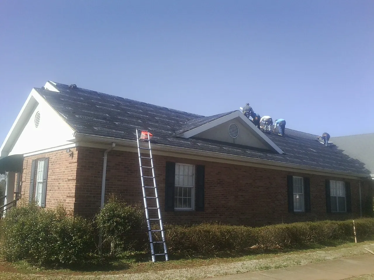 Crew tearing shingles off a brick ranch roof with a ladder set — Emergency Roof Repair work by our crew in Moyock