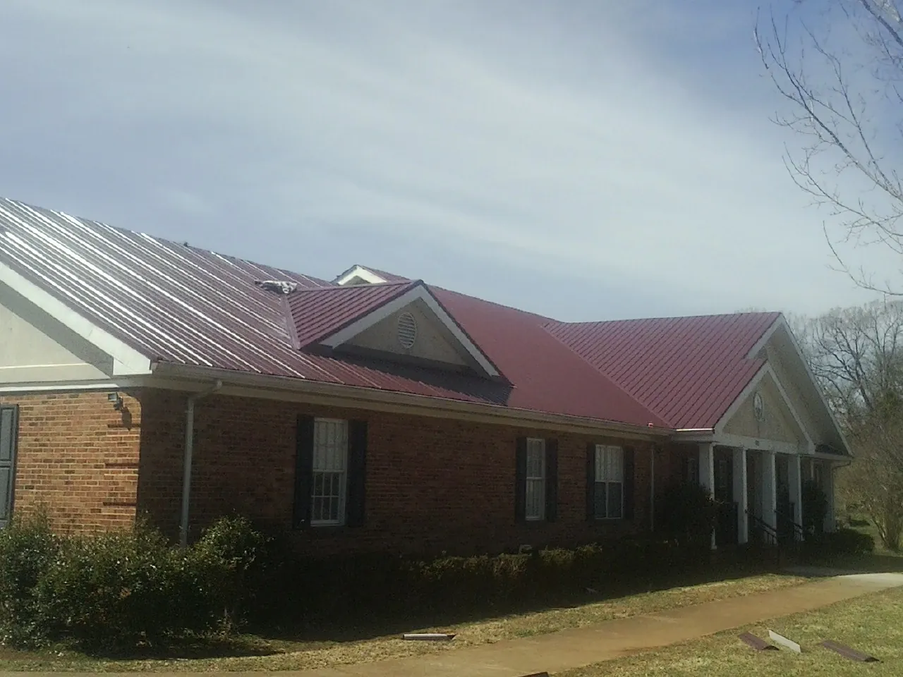 Red metal roof with gabled entries on a long brick building, from a Hail Damage Roof Repair job in Moyock