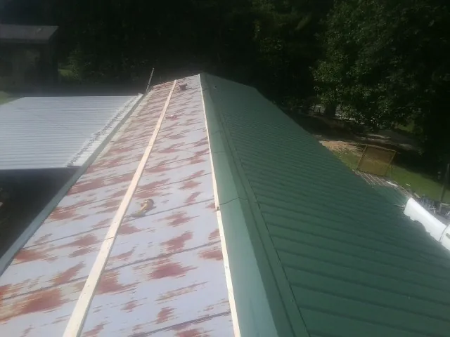 Old rusted panels beside newly installed green metal roofing — Wind Damage Roof Repair by Roofing Brothers in Moyock