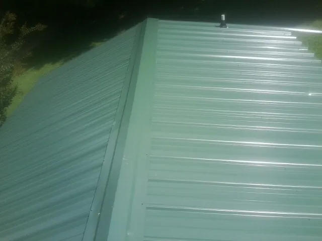 New green metal panels meeting at the ridge of a roof — Flat Roof Repair work by our crew in Moyock
