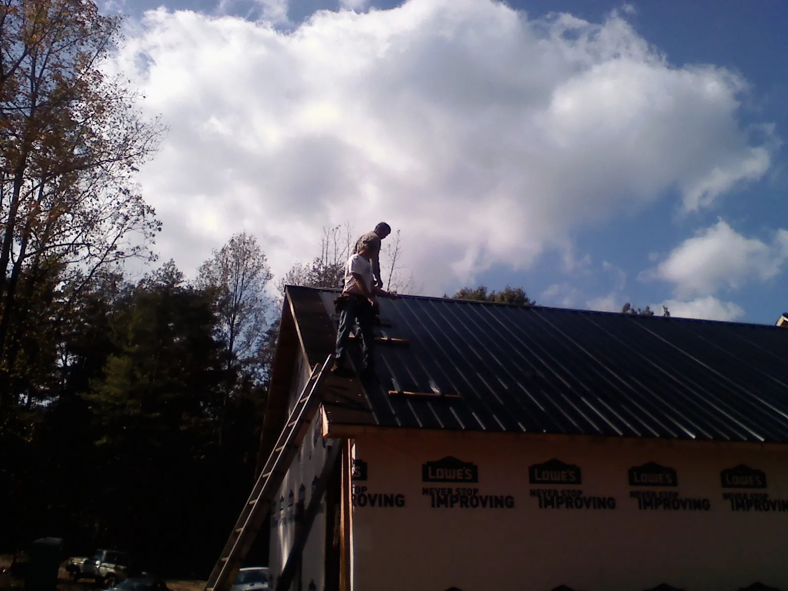 Roofer fastening dark metal panels high against a cloudy sky, from a Roof Inspection job in Moyock