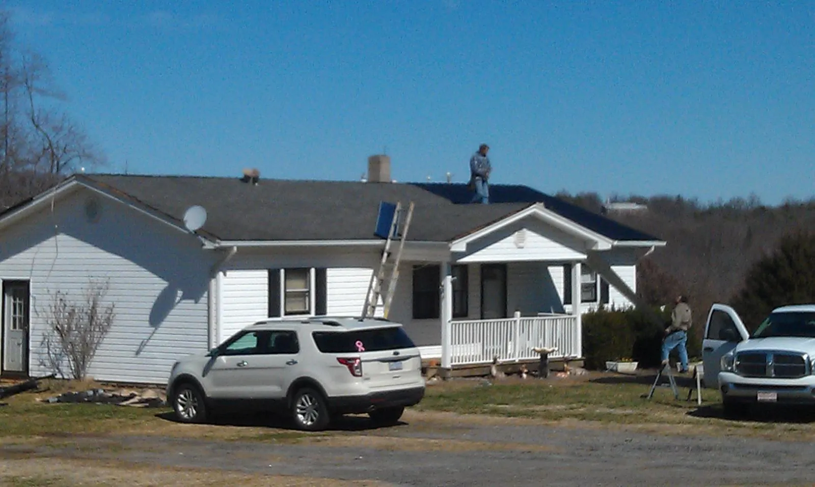 Roofers stripping shingles from a white ranch house roof in Moyock