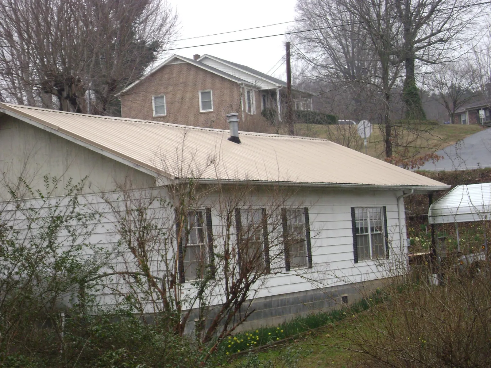 Tan metal roof on a white sided house set into a hillside — Commercial Roofing by Roofing Brothers in Moyock